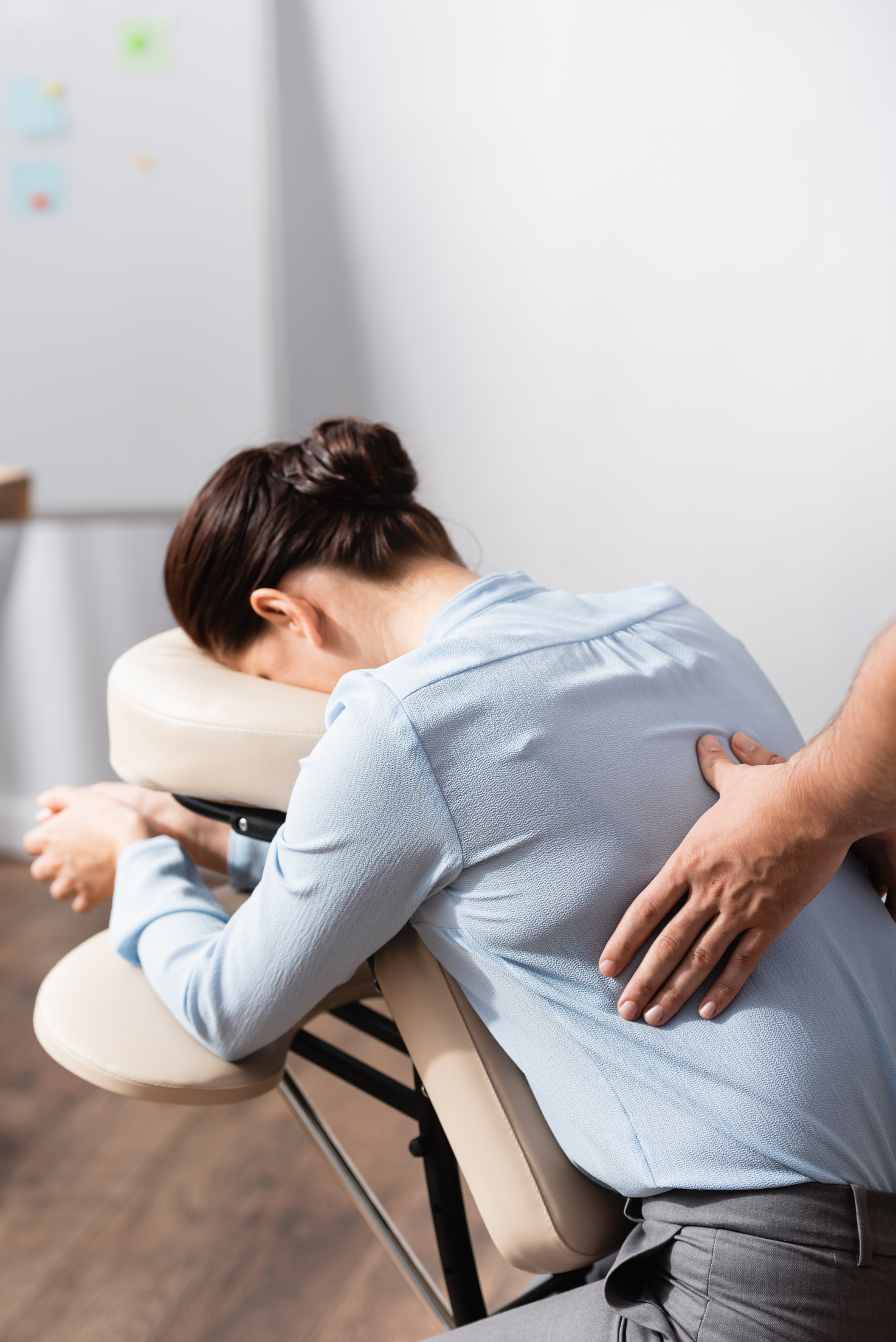 Masseur doing seated massage of back for female client on blurred background